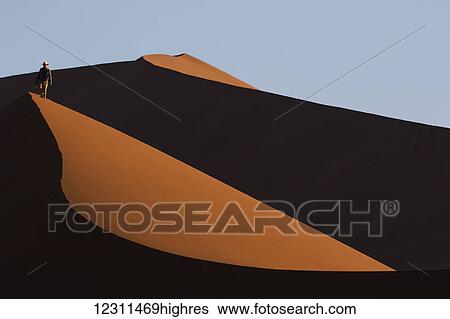 Stock Photograph - Man walking through the sand dunes of the Namib desert in Sossusvlei; Namibia. Fotosearch
