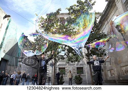 Stock Photograph - Men with large bubbles made with wands in the town square; Barcelona, Catalonia, Spain. Fotosearch