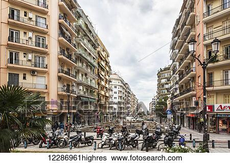 Stock Photograph - Motorcycles parked at the end of a street with residential buildings and shops; Thessaloniki, Greece. Fotosearch