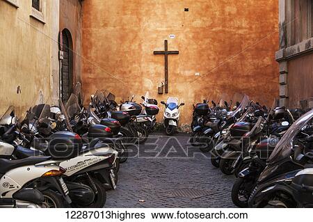 Stock Photograph - Motorcycles parked outside a church with a cross on the wall; Rome, Italy. Fotosearch