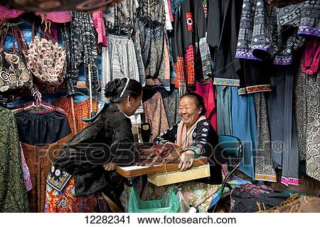 Stock Image - Needlewomen Hmong in front of a display of colorful clothes; Chiang Mai, Thailand. Fotosearch