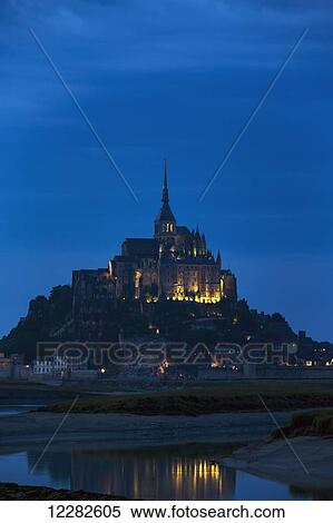 Night image of large stone Abbey perched on rocky island at low tide lit with flood lights with reflection in water; Mont St. Michel, Brittany, France View Large Photo Image Stock Photography - Night image of large stone Abbey perched on rocky island at low tide lit with flood lights with reflection in water; Mont St. Michel, Brittany, France. Fotosearch