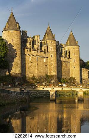 Picture - Old stone castle with large turrets and bridge reflecting off the river at sun set wtih blue sky; Josseline, Brittany, France. Fotosearch