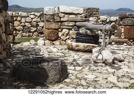Stock Photograph - Olive press and stone basin at the site of ancient ruins; Tel Hazor, Israel. Fotosearch