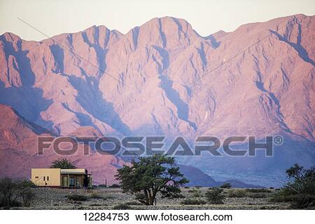 Stock Image - Open landscape with cascading mountains behind a small house; Sossusvlei, Namibia. Fotosearch
