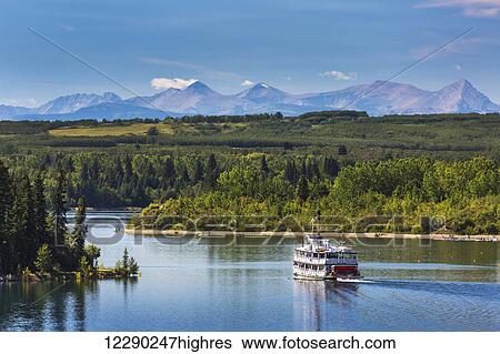 Paddlewheel boat on lake with tree lined shoreline, hills and mountains in the background and blue sky and clouds; Calgary, Alberta, Canada View Large Photo Image Stock Photograph - Paddlewheel boat on lake with tree lined shoreline, hills and mountains in the background and blue sky and clouds; Calgary, Alberta, Canada. Fotosearch