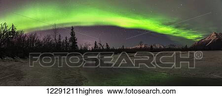 Stock Photograph - Panoramic view of the aurora borealis over the frozen Knik River with Pioneer Peak in the background.. Fotosearch
