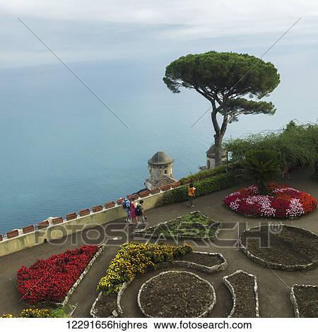 Stock Photograph - Pedestrians along a walkway with colourful flowers in bloom and a view of the ocean; Ravello, Italy. Fotosearch