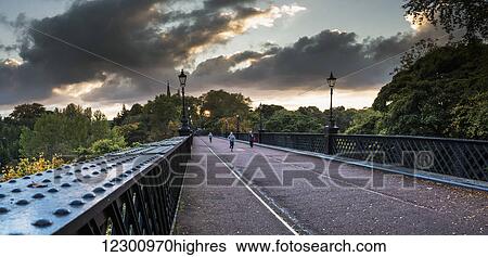 Stock Photograph - Pedestrians and a runner on a bridge with clouds glowing at sunset; Newcastle, Tyne and Wear, England. Fotosearch