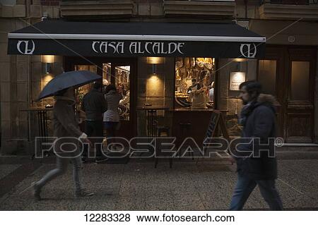 Pedestrians and people entering a bar on Calle Major at dusk, one woman carrying an umbrella; San Sebastian, Spain View Large Photo Image Stock Photo - Pedestrians and people entering a bar on Calle Major at dusk, one woman carrying an umbrella; San Sebastian, Spain. Fotosearch