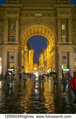 Stock Photograph - Pedestrians on a wet walkway at nighttime with illuminated buildings; Florence, Toscana, Italy. Fotosearch