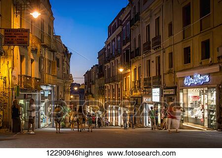 Stock Photograph - Pedestrians on the street in Cagliari at night; Cagliari, Sardinia, Italy. Fotosearch