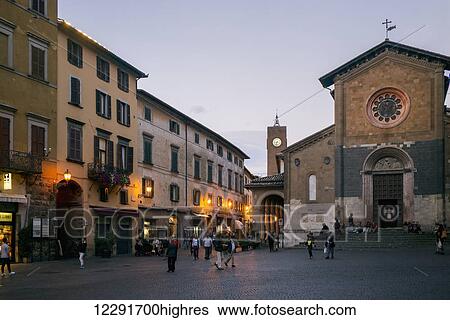 Stock Photograph - Pedestrians walk in a town square with shops and a church at dusk; Orvieto, Umbria, Italy. Fotosearch