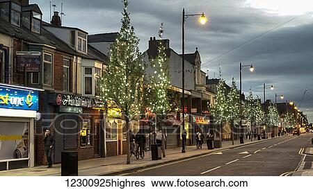 Stock Photograph - Pedestrians walking down a street by shops at dusk; South Shields, Tyne and Wear, England. Fotosearch
