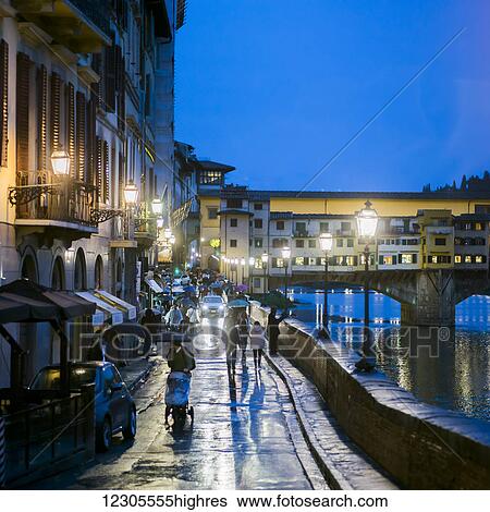 Pedestrians walking on a wet promenade at dusk along the Arno River with a view of Ponte Vecchio; Florence, Italy View Large Photo Image Stock Photograph - Pedestrians walking on a wet promenade at dusk along the Arno River with a view of Ponte Vecchio; Florence, Italy. Fotosearch