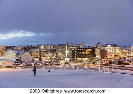 Stock Photograph - People sledding at a hill at Arnarholl Park above the old harbour distict in Reykjavik at twilight; Reykjavik, Iceland. Fotosearch