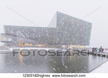 Stock Photograph - People walking outside of the Harpa Public Concert Hall during a Snow Storm, designed by the Danish firm Henning Larsen Architects and Icelandic firm Batteriao Architects, the glass facade is designed by Icelandic artist Olafur Eliasson; Reykjavik,.... Fotosearch