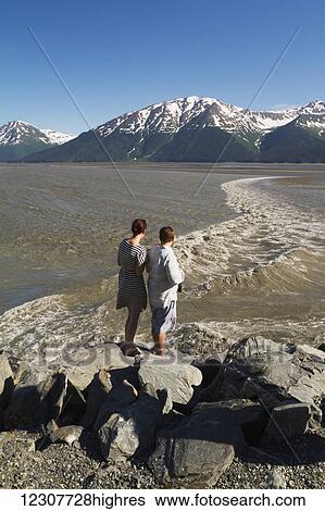 Stock Photograph - People watching the bore tide in Turnagain Arm. They are at Mile 94 of the Seward Highway at a pull-off. Spring. Southcentral Alaska.. Fotosearch