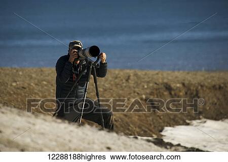 Stock Photograph - Photographer with camera on tripod with long lens and Arctic ocean in the background; Spitsbergen, Svalbard, Norway. Fotosearch