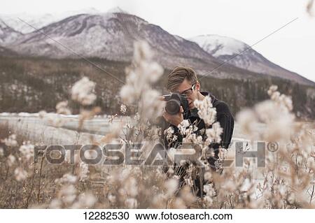 Stock Image - Photographer with camera raised to take a picture of autumn foliage and standing in a field, Alaska, Autumn . Fotosearch