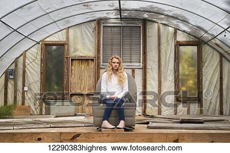 Stock Photograph - Portrait of a caucasian teenage girl with long blond curly hair sitting in a grey recliner in a greenhouse; Apex, North Carolina, United States of America. Fotosearch