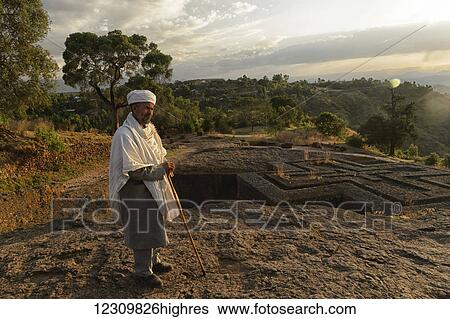 Stock Photograph - Priest standing outside an underground stone church; Lalibela, Ethiopia. Fotosearch