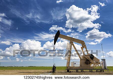 Stock Photograph - Pump jack in a field with large puffy clouds and blue sky; Alberta, Canada. Fotosearch