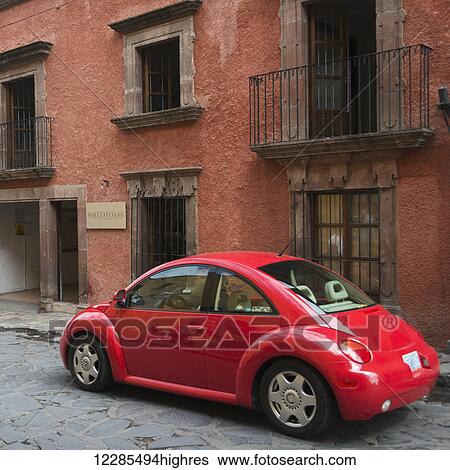 Stock Photograph - Red car parked outside a residential building; San Miguel de Allende, Guanajuato, Mexico. Fotosearch