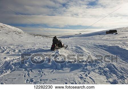 Stock Image - Riding across the frozen tundra on a snow machine, cabin in the distance; Cambridge Bay, Nunavut, Canada. Fotosearch