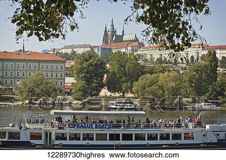 Stock Photograph - River boat tour with tourists travels down the Vlatava river; Prague, Czech Republic. Fotosearch