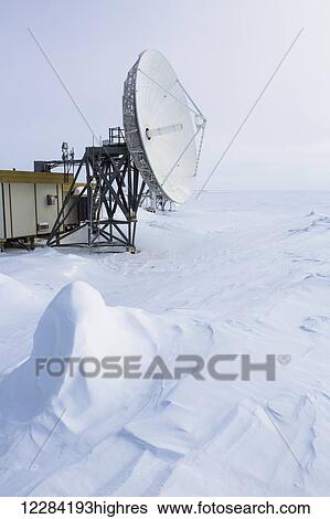 Stock Photograph - Satellite dish points out to barren sea ice, snow drifts carved by the wind in the foreground, Barrow, North Slope, Arctic Alaska, USA, Winter. Fotosearch