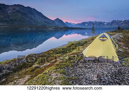 Stock Photograph - Scenic view of Lower Twin Lake with a backpacking tent in the foreground and sunset, Lake Clark National Park & Preserve, Southcentral Alaska. Fotosearch