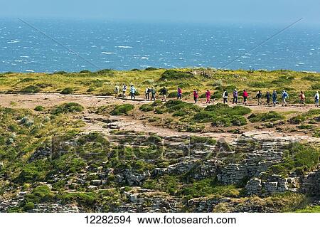 Picture - Several walkers along a stone pathway overlooking the sea with blue sky; Frehal, Brittany, France. Fotosearch