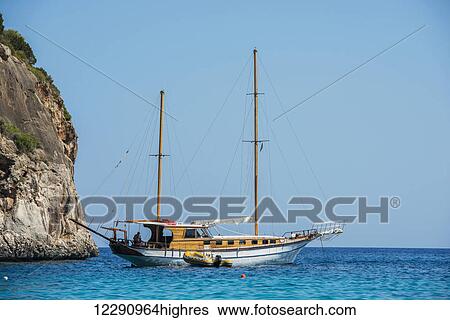 Stock Photograph - Ship beside a cliff along the coast of the Mediterranean; Cala Gonone, Sardinia, Italy. Fotosearch