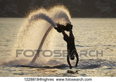Stock Photograph - Silhouette of backlit flyboarder diving vertically with arms stretched out; Torba, Mugla Province, Turkey. Fotosearch