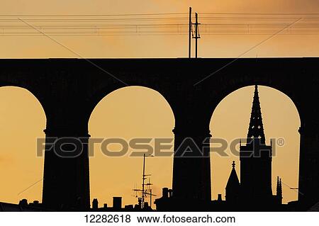 Stock Photo - Silhouette of large viaduct and church steeple with an orange sky at sunset; Morlaix, Brittany, France. Fotosearch