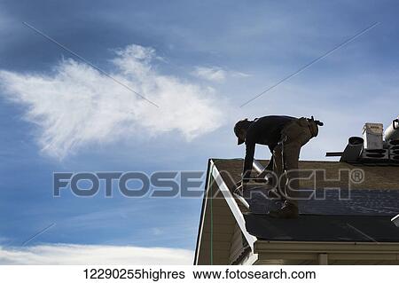 Silhouette of male roofer on top of roof stapling tar paper with clouds and blue sky; Calgary, Alberta, Canada View Large Photo Image Stock Photograph - Silhouette of male roofer on top of roof stapling tar paper with clouds and blue sky; Calgary, Alberta, Canada. Fotosearch
