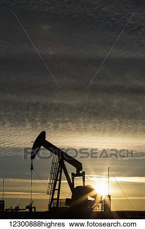 Silhouette of pump jack at sunrise with sun burst and colourful clouds in the sky; Alberta, Canada View Large Photo Image Stock Photograph - Silhouette of pump jack at sunrise with sun burst and colourful clouds in the sky; Alberta, Canada. Fotosearch