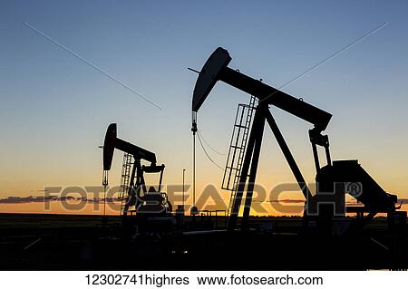 Silhouette of two pump jacks at sunrise with orange glow in the sky and clouds; Acme, Alberta, Canada View Large Photo Image Stock Photograph - Silhouette of two pump jacks at sunrise with orange glow in the sky and clouds; Acme, Alberta, Canada. Fotosearch