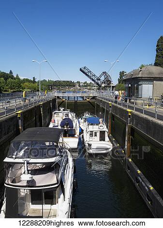 Stock Photograph - Small boats float in a lock, a draw bridge in the background, Ballard Locks, Seattle, Washington, USA, Summer. Fotosearch