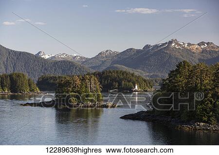 Stock Photograph - Small islands populated by Sitka spruce trees, a lighthouse in the background; Sitka, Alaska, United States of America. Fotosearch