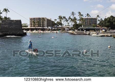 Stock Photograph - Stand up paddleboarding in front of the King Kam hotel; Kailua-Kona, Island of Hawaii, Hawaii, United States of America. Fotosearch