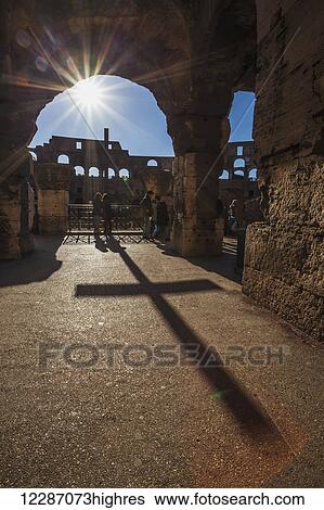 Stock Photograph - Sunburst through an archway at the Colosseum and a shadow of a cross; Rome, Italy. Fotosearch