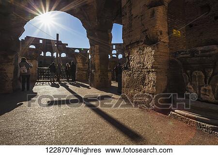 Stock Photograph - Sunburst through an archway at the Colosseum and a shadow of a cross; Rome, Italy. Fotosearch