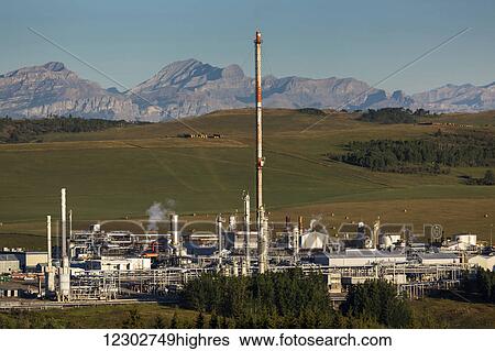 Stock Photograph - Sunrise light on a gas plant with large stack and mountains and foothills in the background; Alberta, Canada. Fotosearch