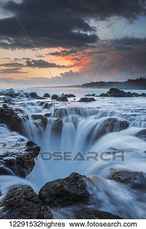 Stock Photograph - Surf spills into a hole in a rock shelf along the coast in northeastern Kauai; Kauai, Hawaii, United States of America. Fotosearch
