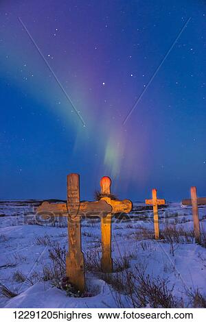Stock Photograph - The aurora borealis colors the sky above crosses catching the light of dusk at Cemetery Hill in Kotzebue, Alaska.. Fotosearch
