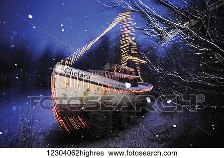 Stock Photograph - The Chelsea, a double-ender boat is outlined in Christmas lights during a snowfall along East End Road in Homer, Alaska, USA. Fotosearch