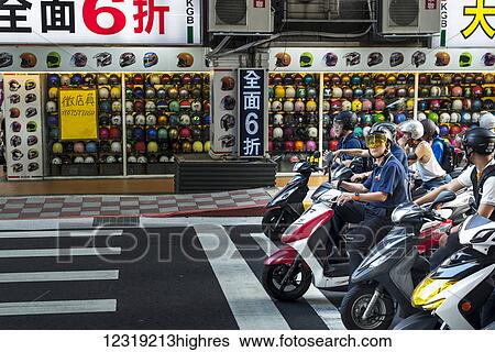 Stock Photograph - The motorbikes and scooters in Taibei city are really a big number, helmet shop in view with scooters stopped on the road; Taiwan, China. Fotosearch