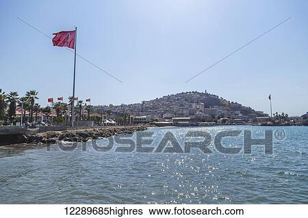 Stock Photograph - The Turkish flag flies in a blue sky on a sunny day next to the Mediterranean sea; Kusadasi, Izmir, Turkey. Fotosearch